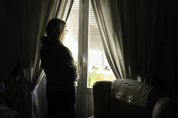 senior woman in very dark room looking out window - major depression