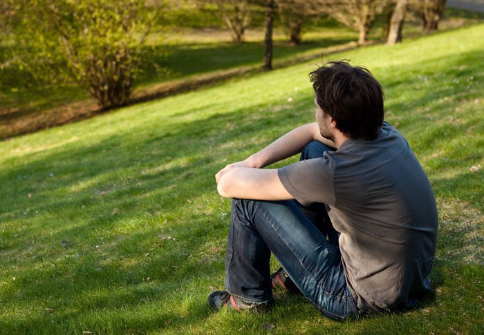 young man sitting on grassy hill outside enjoying nature - spirituality