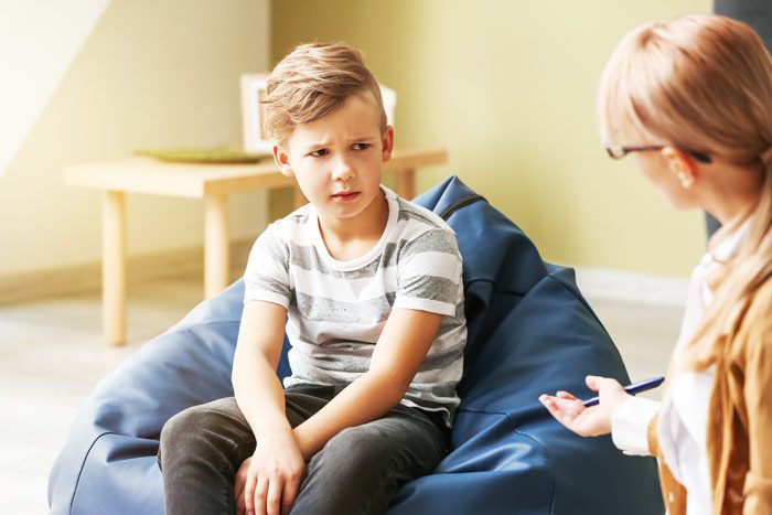 young man of age six to eight sitting on a bean bag, looking quizzically at his therapist - child mental health
