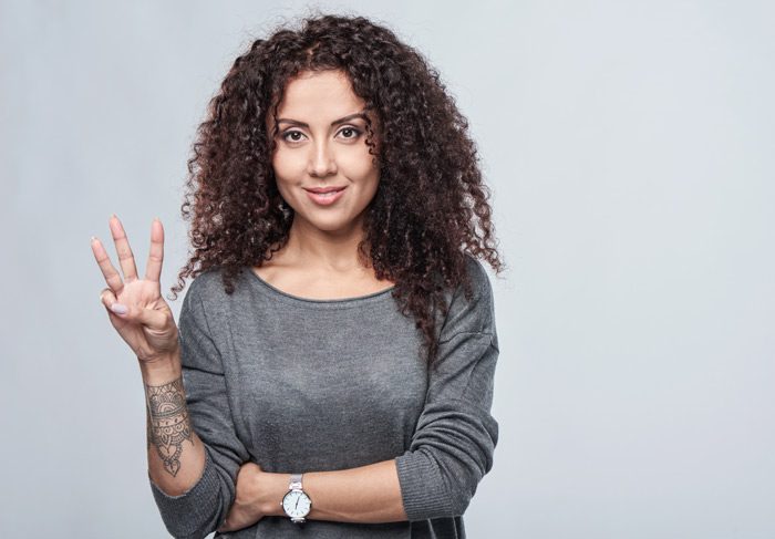 pretty woman holding up three fingers against a light gray background - mental well-being