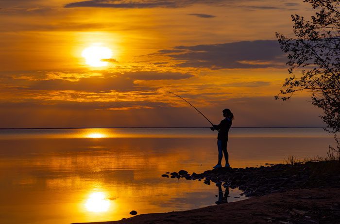 silhouette of a woman fishing during bright orange sunset - relaxation