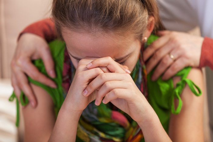 cropped shot of upset teenage girl whose mom's hands are on her shoulders as she cries - child's mental health