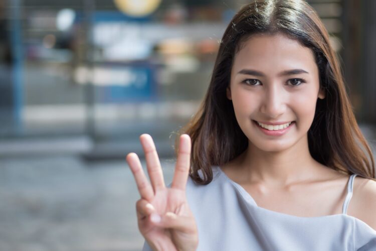 happy girl pointing up number 3 fingers; portrait of joyful happy smiling asian woman pointing hand with three fingers up; concept of number three, 3 points, third place; asian woman young adult model