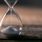 Close-up of an hourglass with white sand falling through, placed on a wooden surface