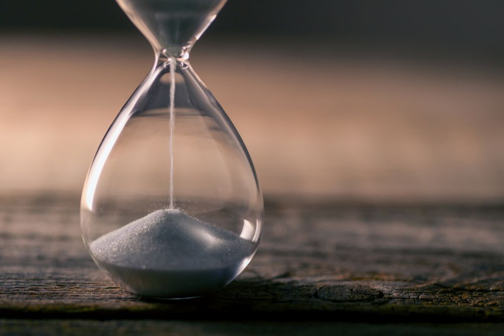 Close-up of an hourglass with white sand falling through, placed on a wooden surface