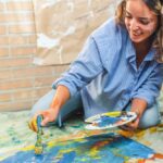 A young girl with paintbrush in hand and a palette of colors immersed in the creative painting process. Against a background of canvas and paints