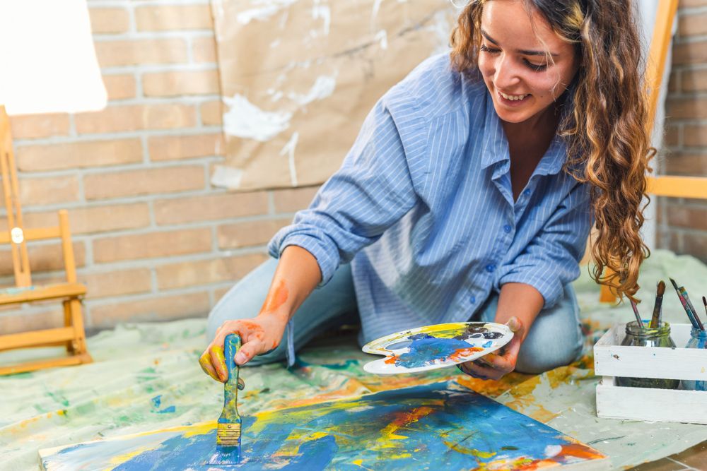 A young girl with paintbrush in hand and a palette of colors immersed in the creative painting process. Against a background of canvas and paints