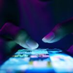 Close-up of a person’s hands scrolling on a smartphone screen glowing with colorful app icons in a dark environment.