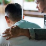 Man offering comfort by placing a supportive hand on another man’s shoulder, symbolizing empathy, emotional support, and caring connection.