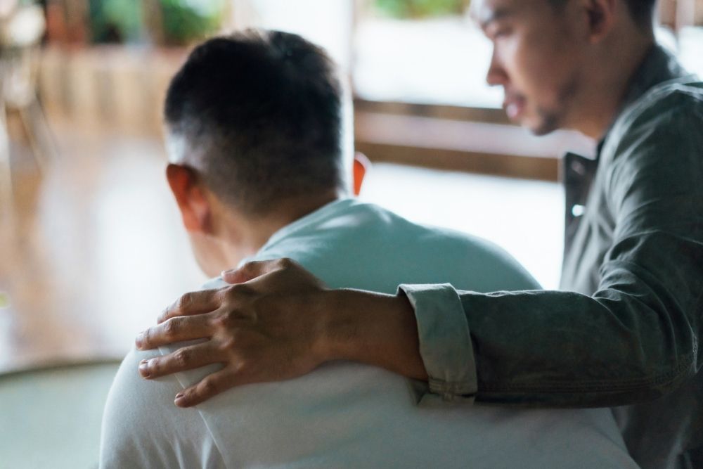 Man offering comfort by placing a supportive hand on another man’s shoulder, symbolizing empathy, emotional support, and caring connection.