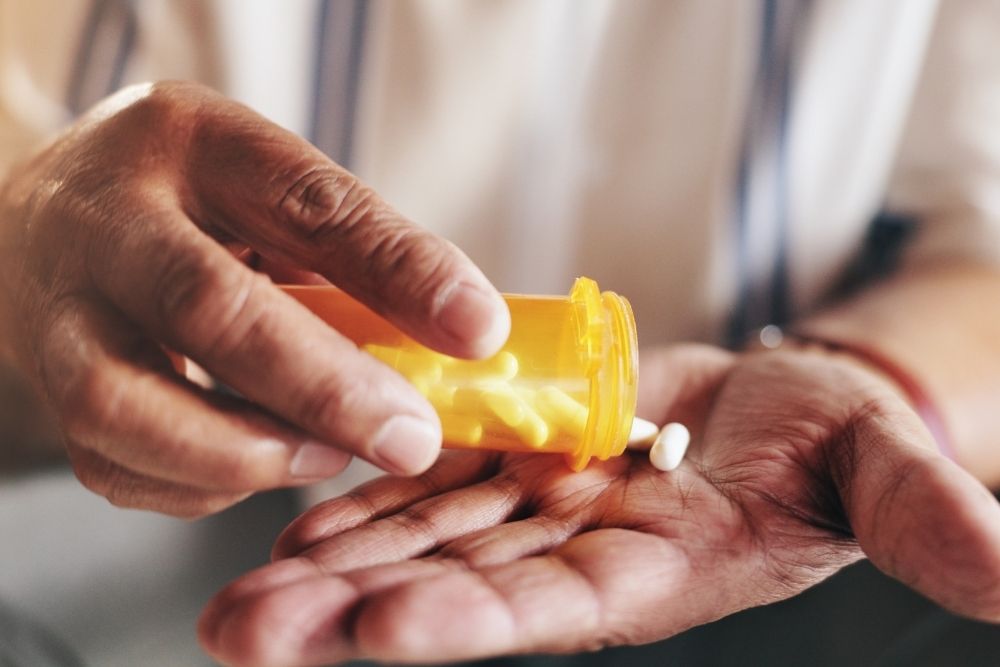 Close-up of hands pouring pills from an orange prescription bottle into an open palm.